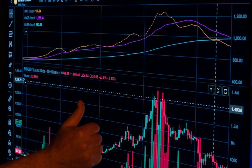 A hand giving a thumbs up in front of a financial graph displaying market trends.